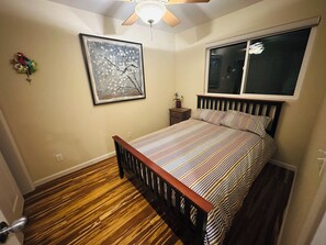 A bedroom with a wooden floor, a bed with striped bedding, a ceiling fan, a window, and a framed picture on the wall. - Charming & Central 2200 sq. feet house in Davis walking distance to everywhere (Davis)