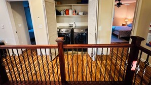 A laundry room with a washing machine and dryer, a small kitchen area, and a bedroom with a bed and nightstand.