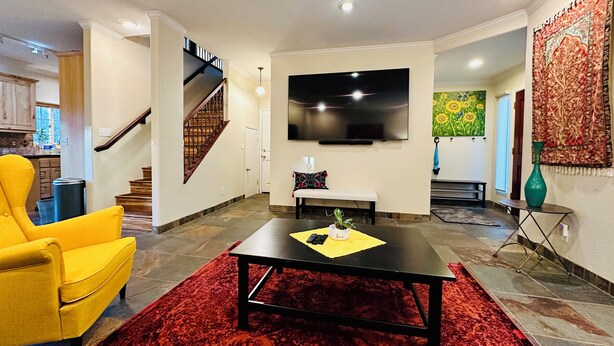 A living room with a red carpet, a yellow armchair, a black coffee table, a TV, and a staircase.