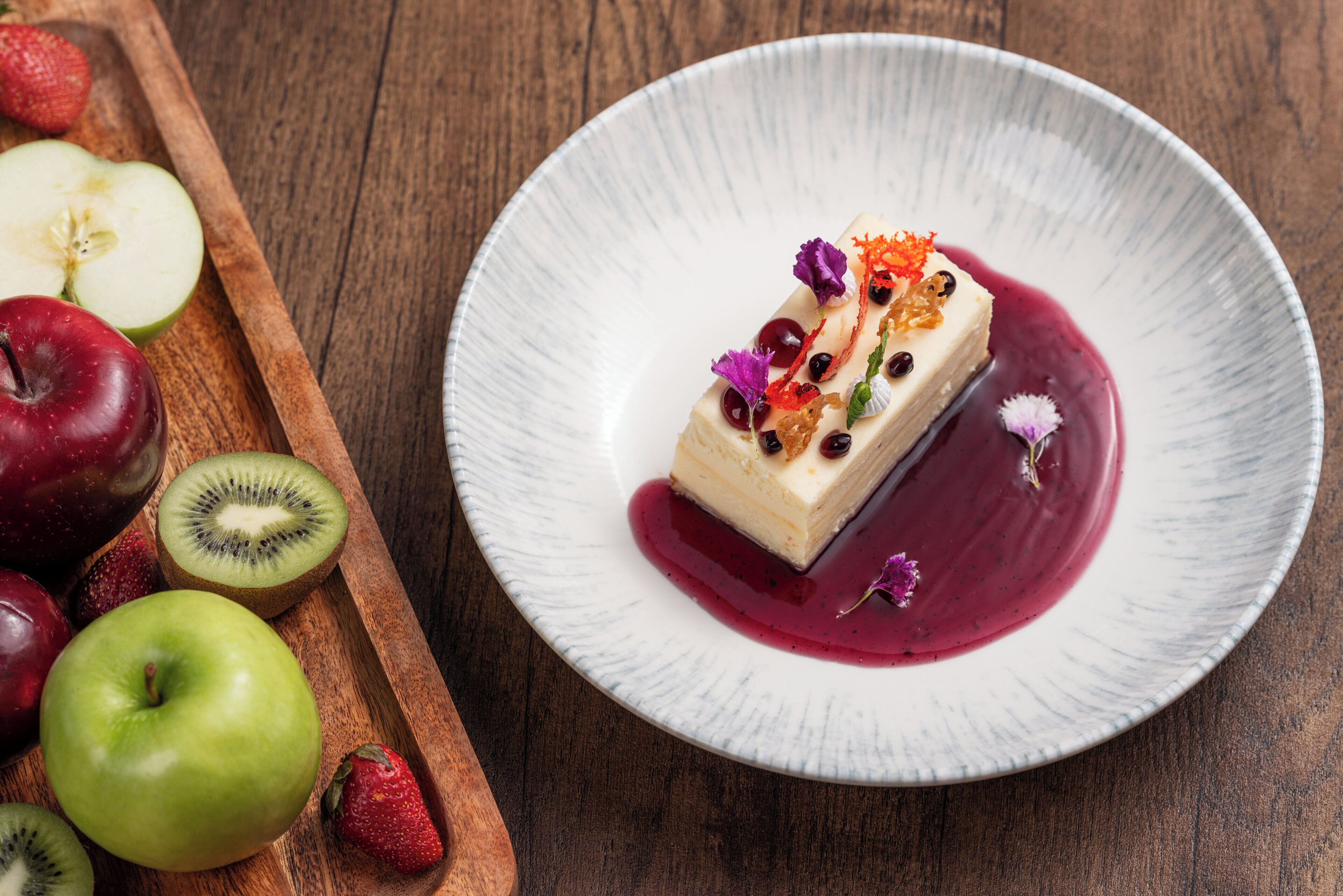 Un dessert présenté sur une assiette, avec un plateau en bois rempli de fruits à côté.