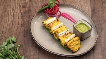 A plate with paneer tikka, a red onion pickle, and a green chutney on a wooden table.
