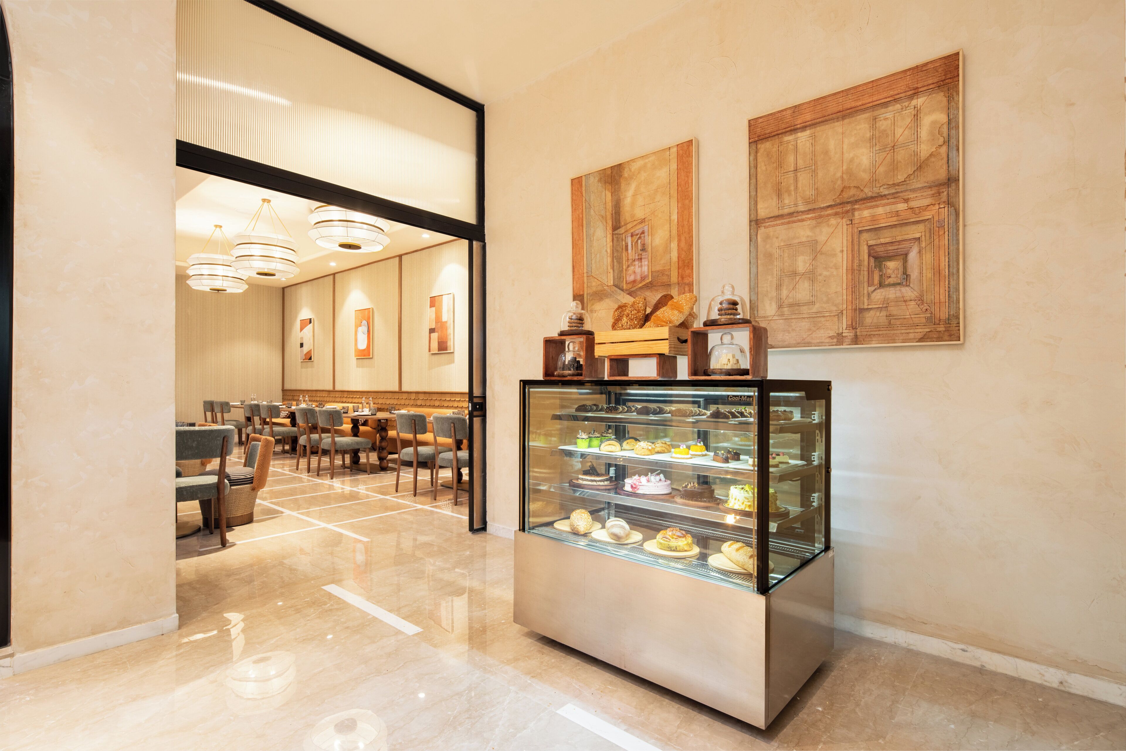 A hotel lobby with a glass display case of pastries, a seating area with tables and chairs, and artwork on the walls.