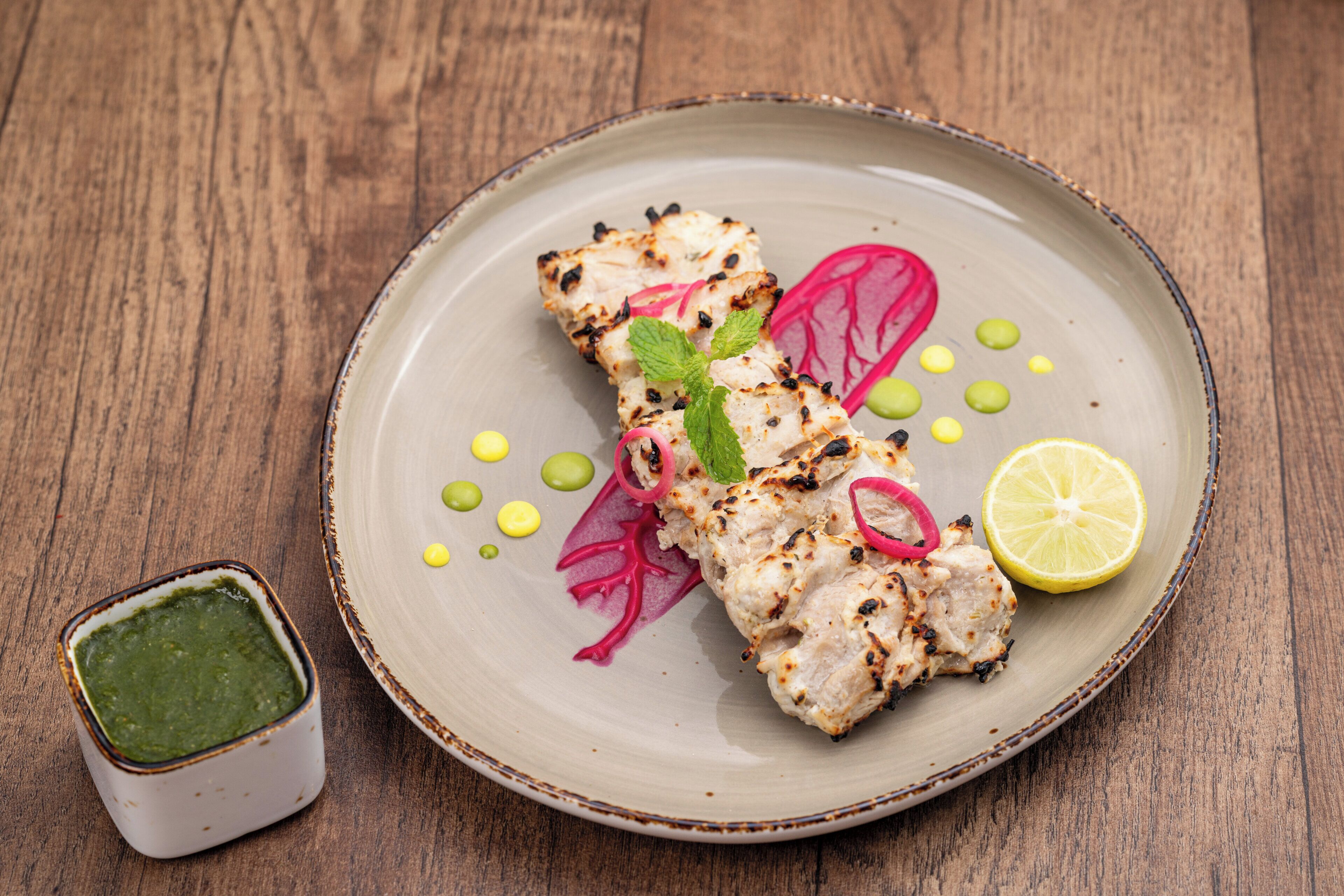 A plate of grilled chicken with vegetables and a lemon wedge on a wooden table.