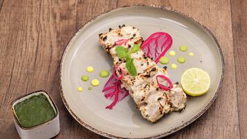 A plate of grilled chicken with vegetables and a lemon wedge on a wooden table.