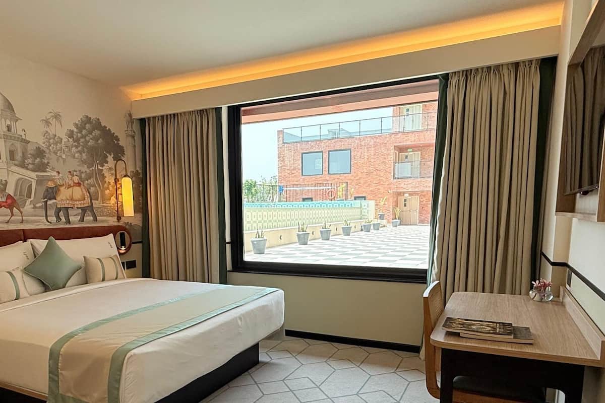 Habitación de hotel con una cama grande, un escritorio, una ventana con cortinas y un mural en la pared.