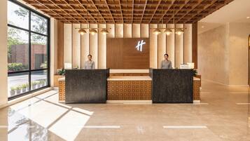 A reception area with a modern design, featuring a wooden ceiling, large windows, and two receptionists at the counter.