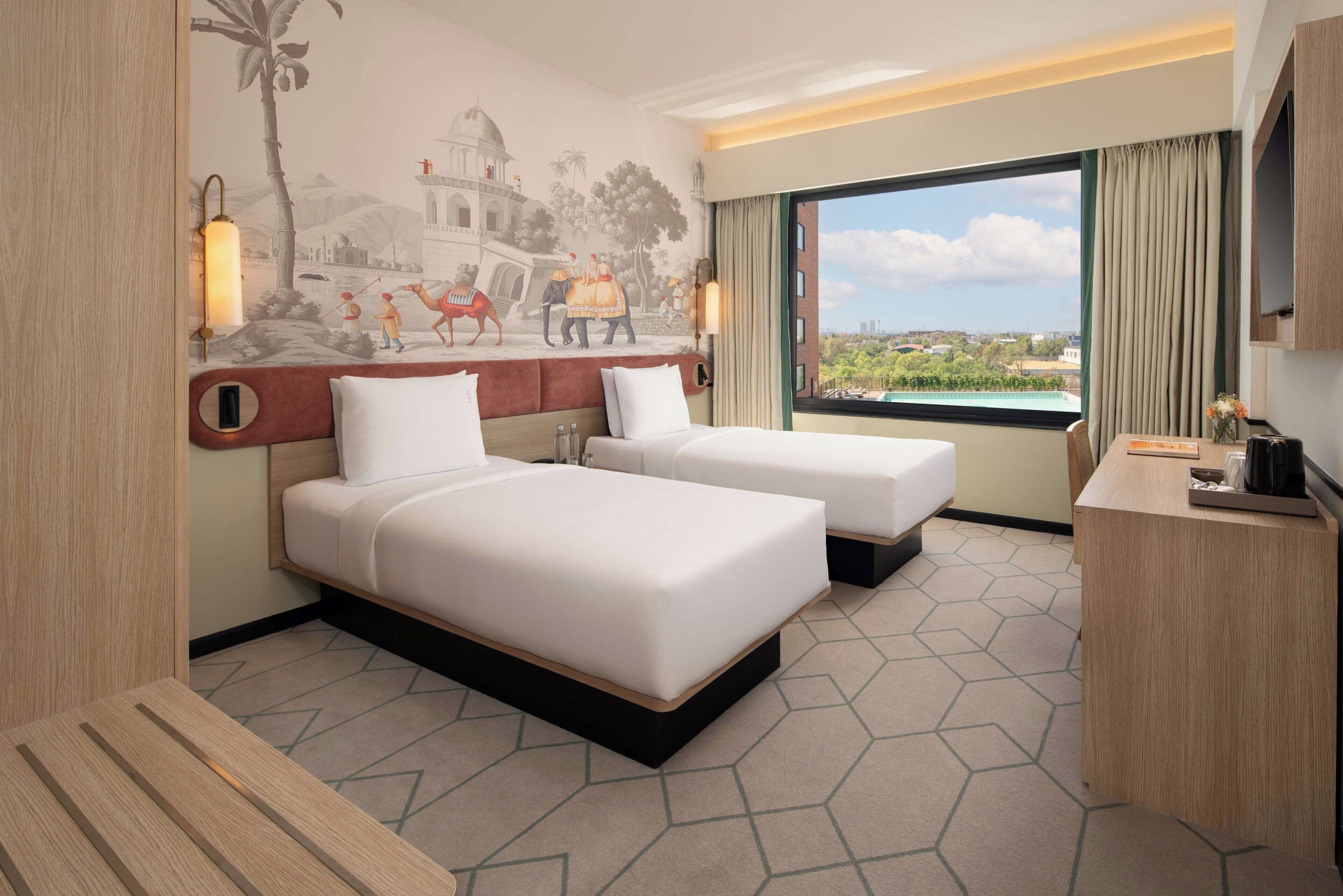 Een hotelkamer met twee bedden, een bureau, een televisie en een muurschildering van een historisch tafereel.
