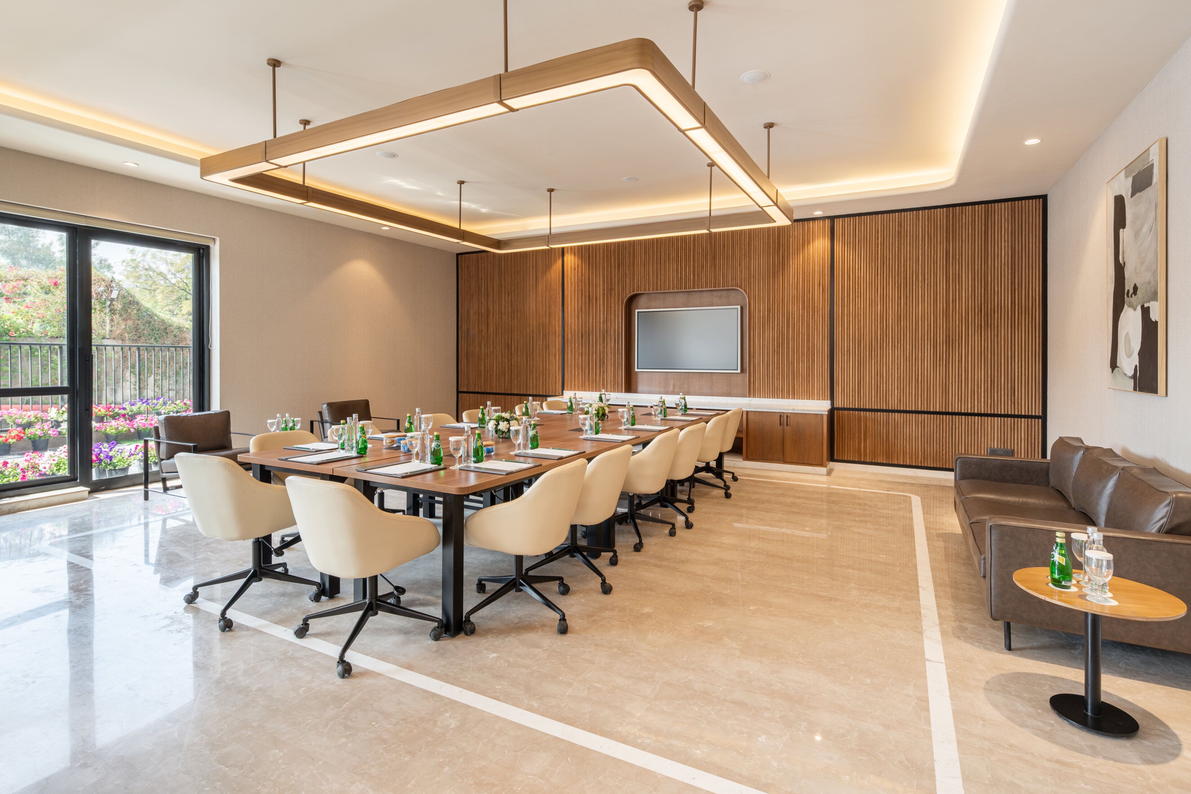 A modern conference room with a long table, chairs, a TV screen, and a sofa.