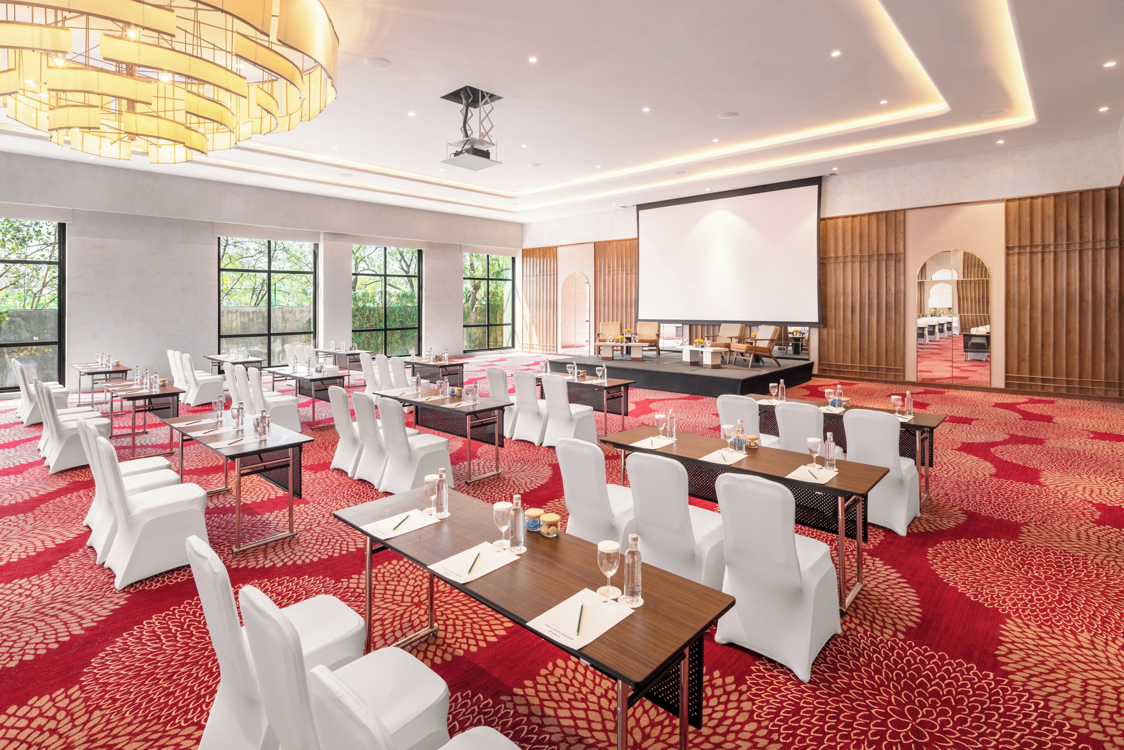 A conference room with white chairs, tables, and a large screen.