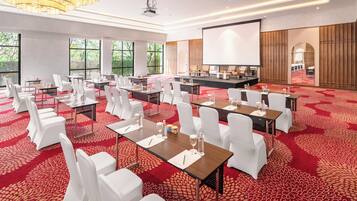 A conference room with white chairs, tables, and a large screen.