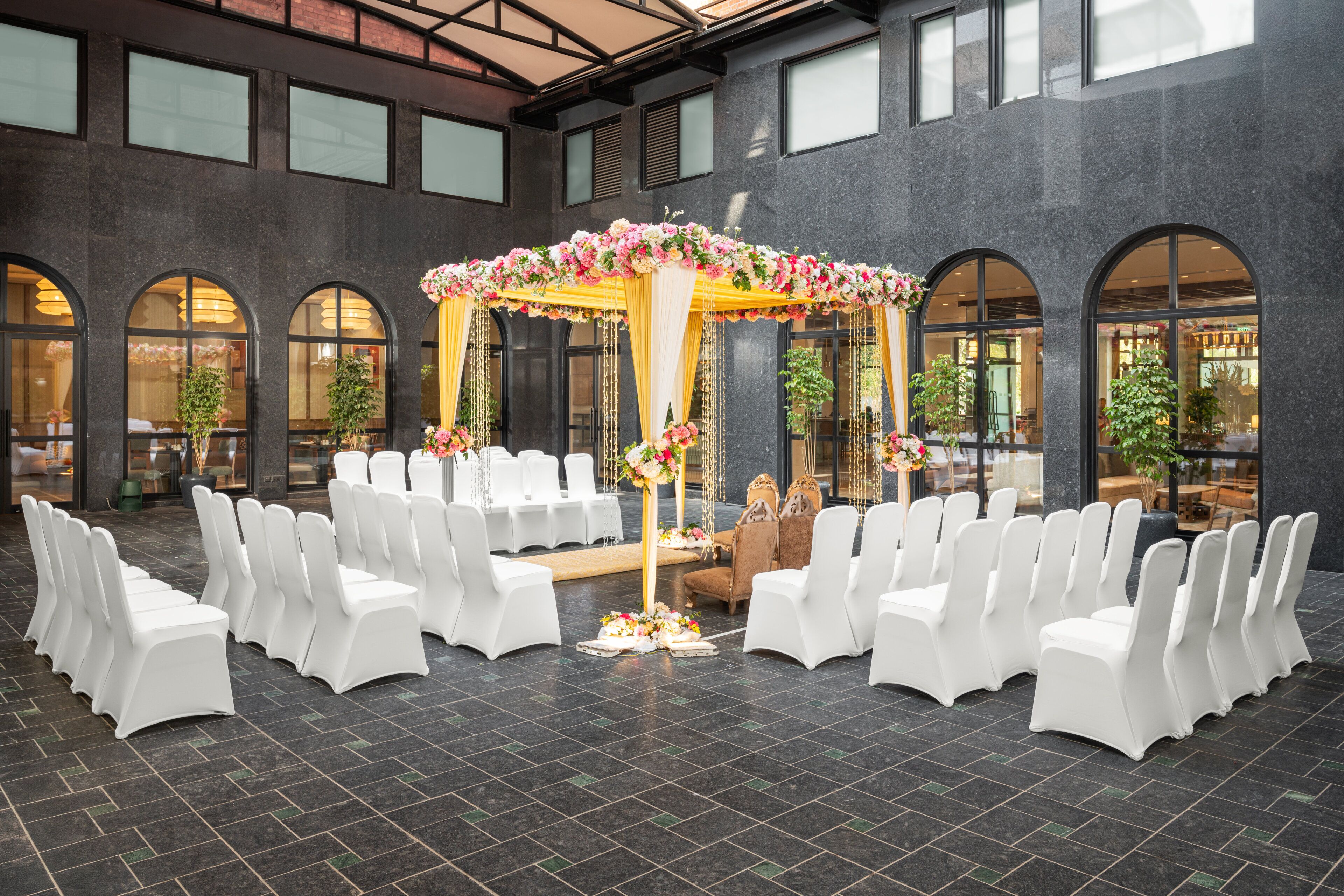 A wedding ceremony setup with white chairs arranged in rows, a floral arch, and a central table with floral arrangements.