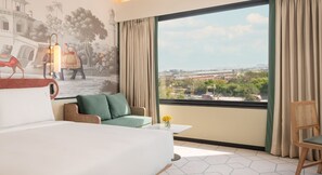 A hotel room with a large bed, a sofa, a chair, a small table, and a mural of a historical scene. - Holiday Inn Gurgaon NH8 by IHG (Gurugram)