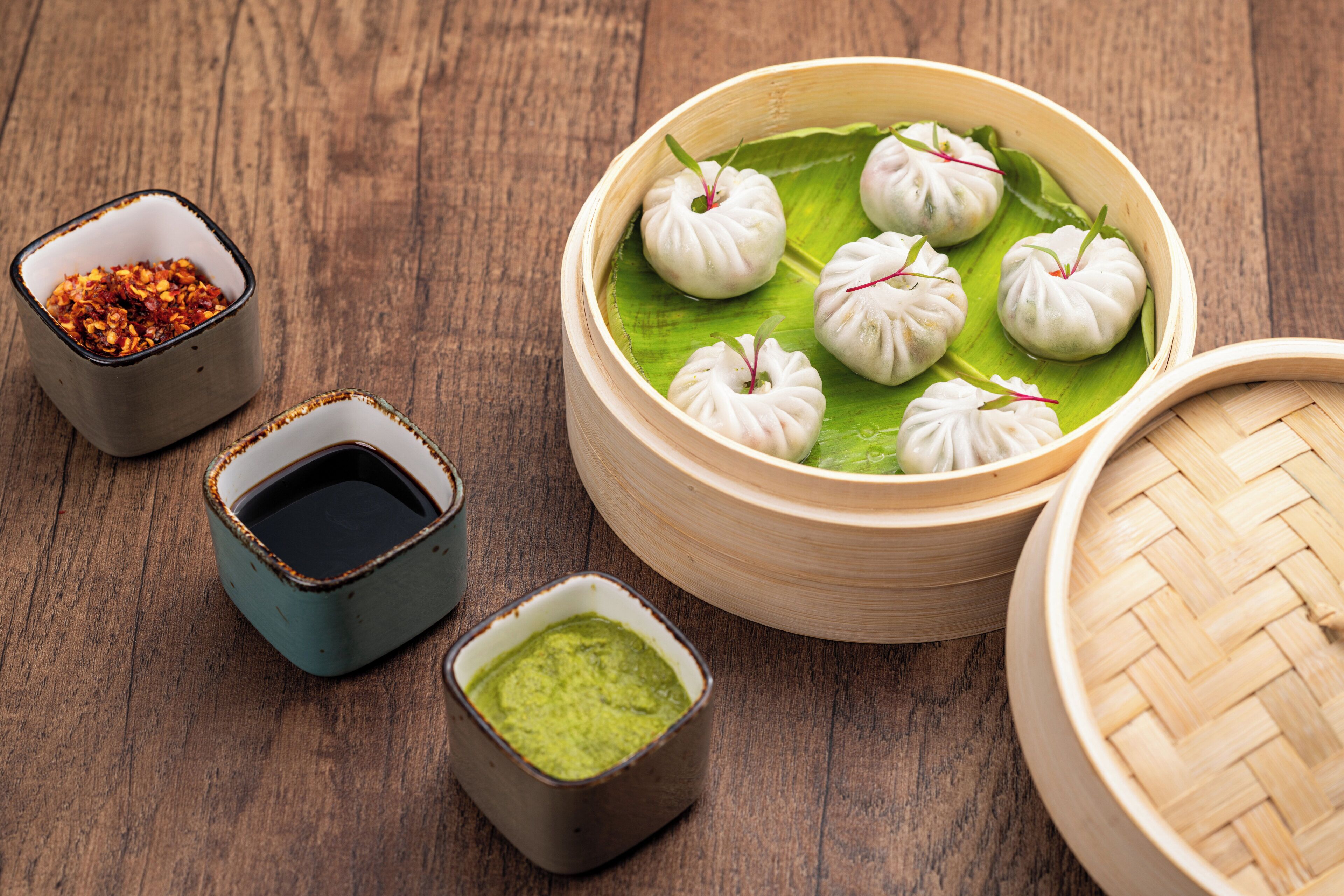 Een bamboestoommandje met dumplings op een blad, vergezeld van twee kleine schaaltjes saus.