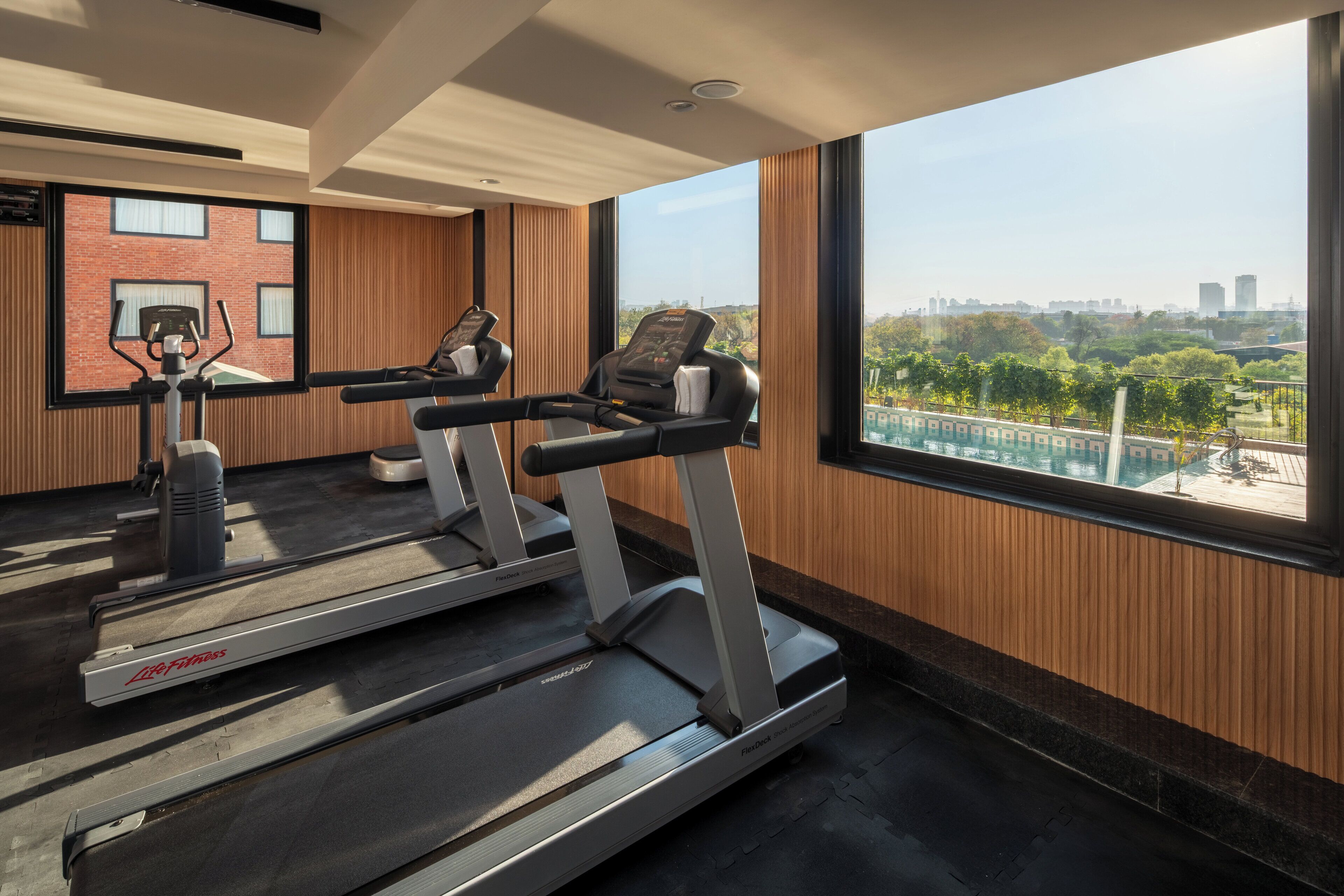 Un gimnasio moderno con cintas de correr y equipo de ejercicio, amplias ventanas con vistas a la ciudad.