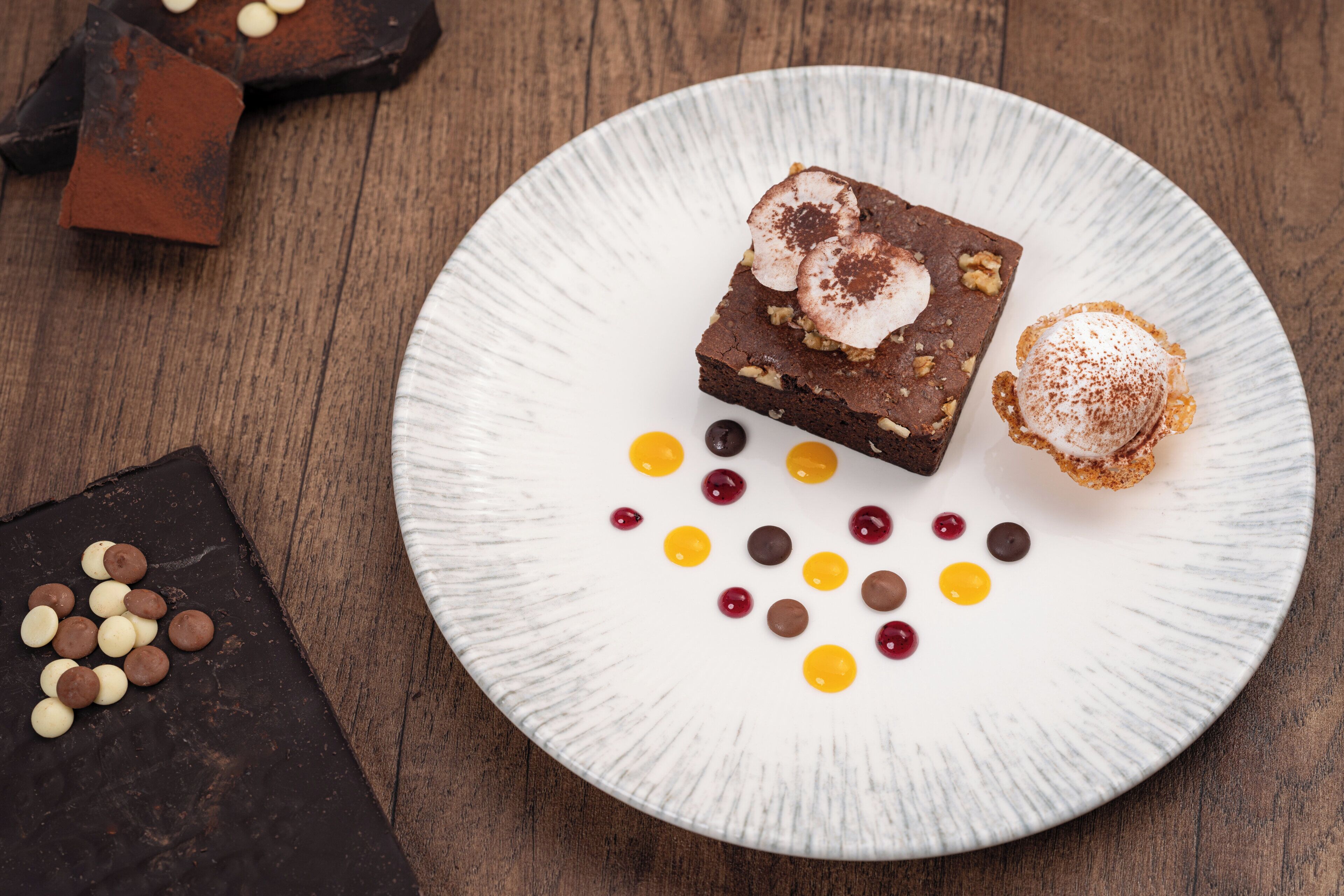 Un plato con un brownie, una bola de helado y varios caramelos sobre una fuente blanca.