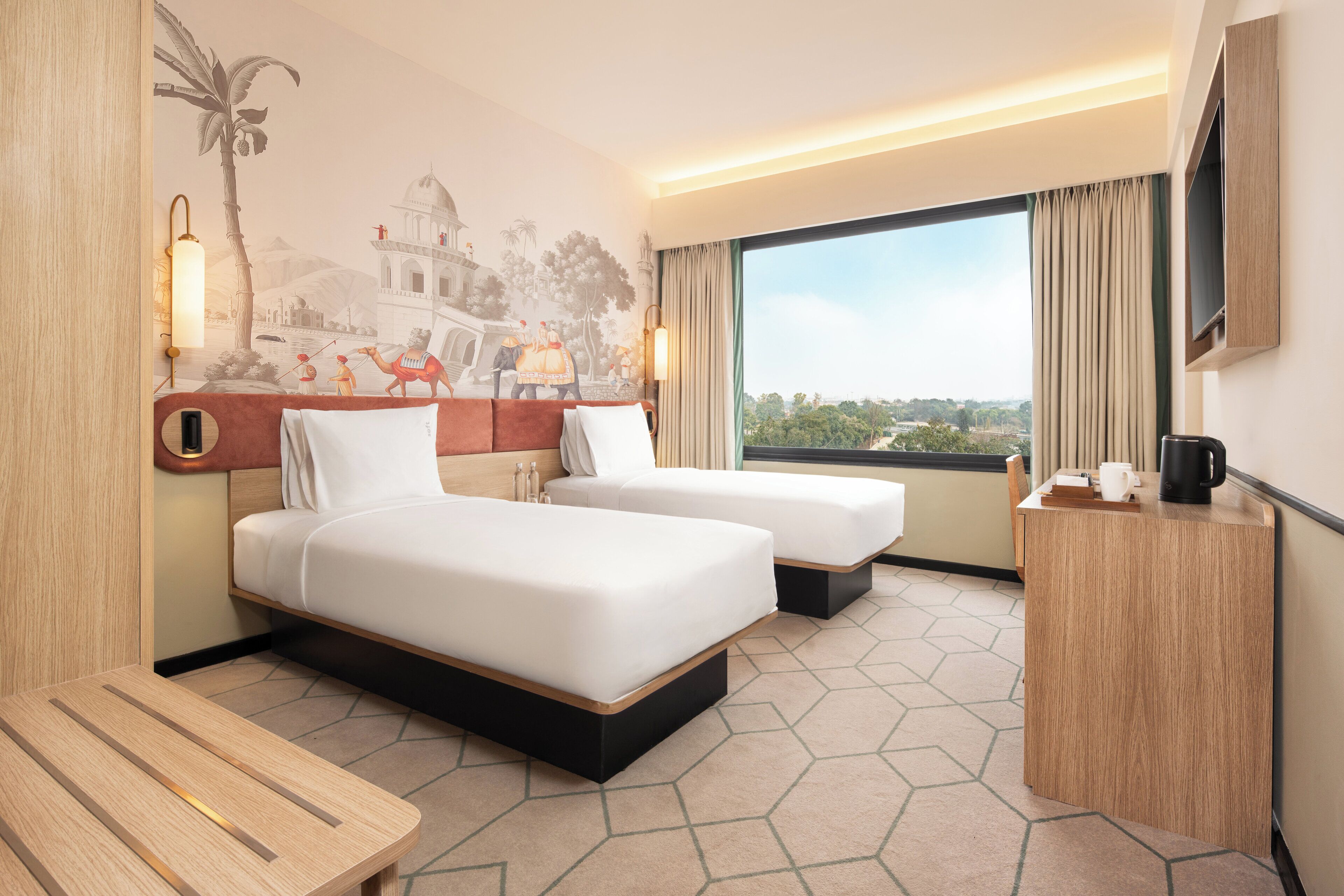 A hotel room with two beds, a wooden desk, a wall-mounted TV, and a large window with a view.