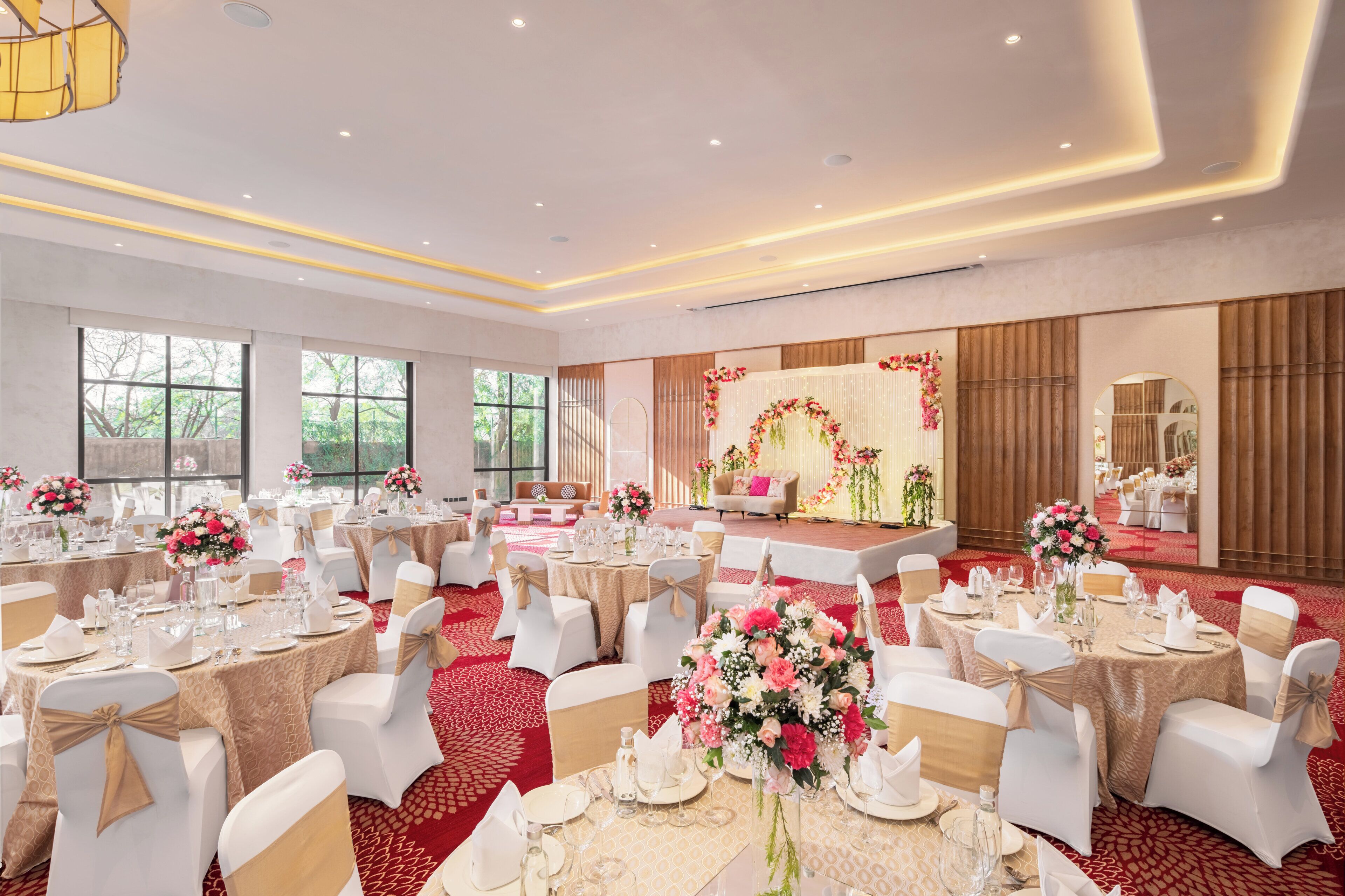 Ein Festsaal mit runden Tischen, weißen Stühlen und floralen Tischdekorationen.