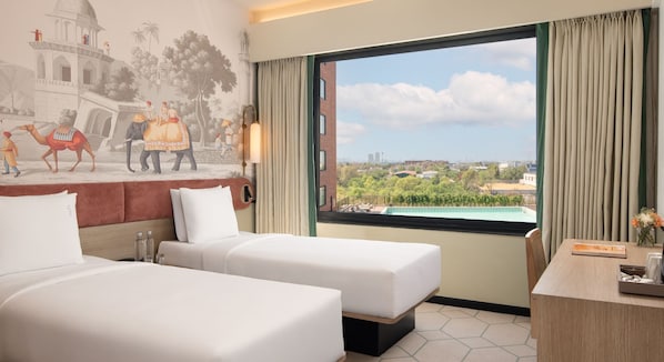 A hotel room with two beds, a mural depicting a historical scene, a large window with a city view, and a desk with a vase of flowers.
