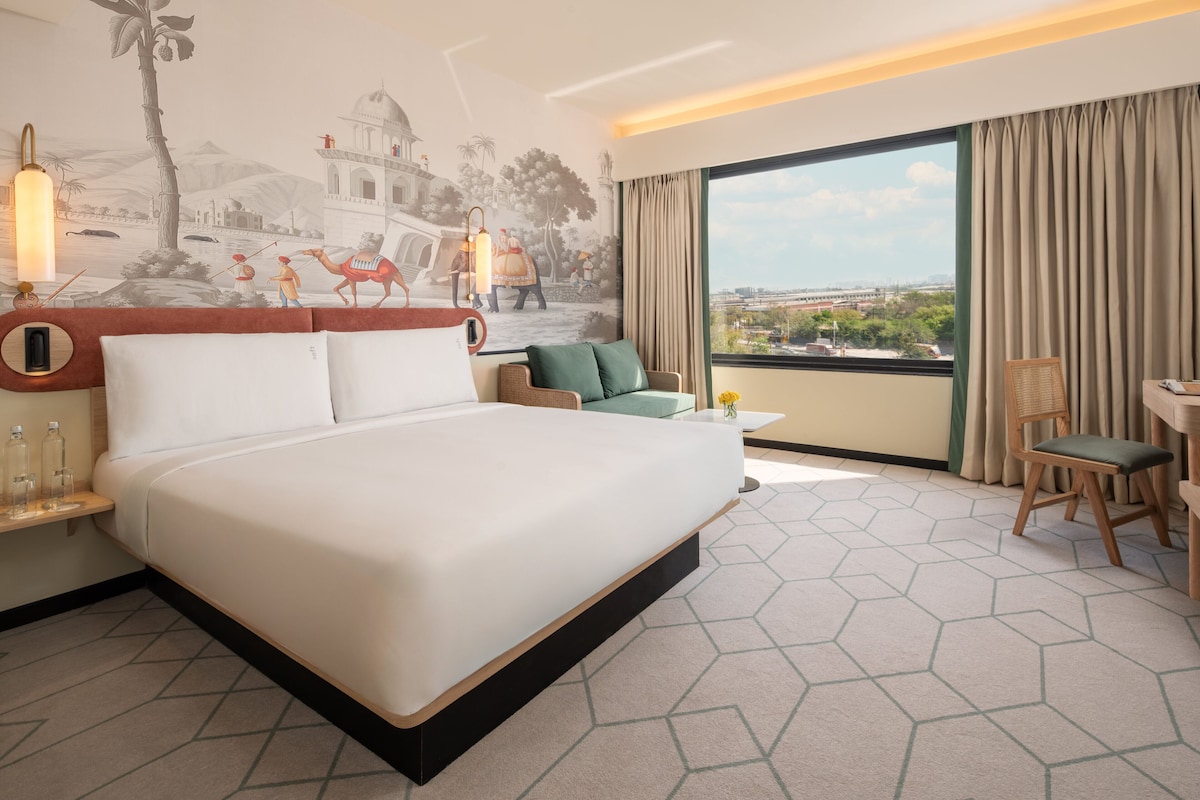 A hotel room with a large bed, a small sofa, a desk, and a view of the city.