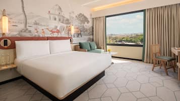 A hotel room with a large bed, a small sofa, a desk, and a view of the city.