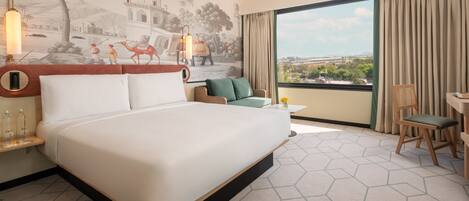 A hotel room with a large bed, a small sofa, a desk, and a view of the city.