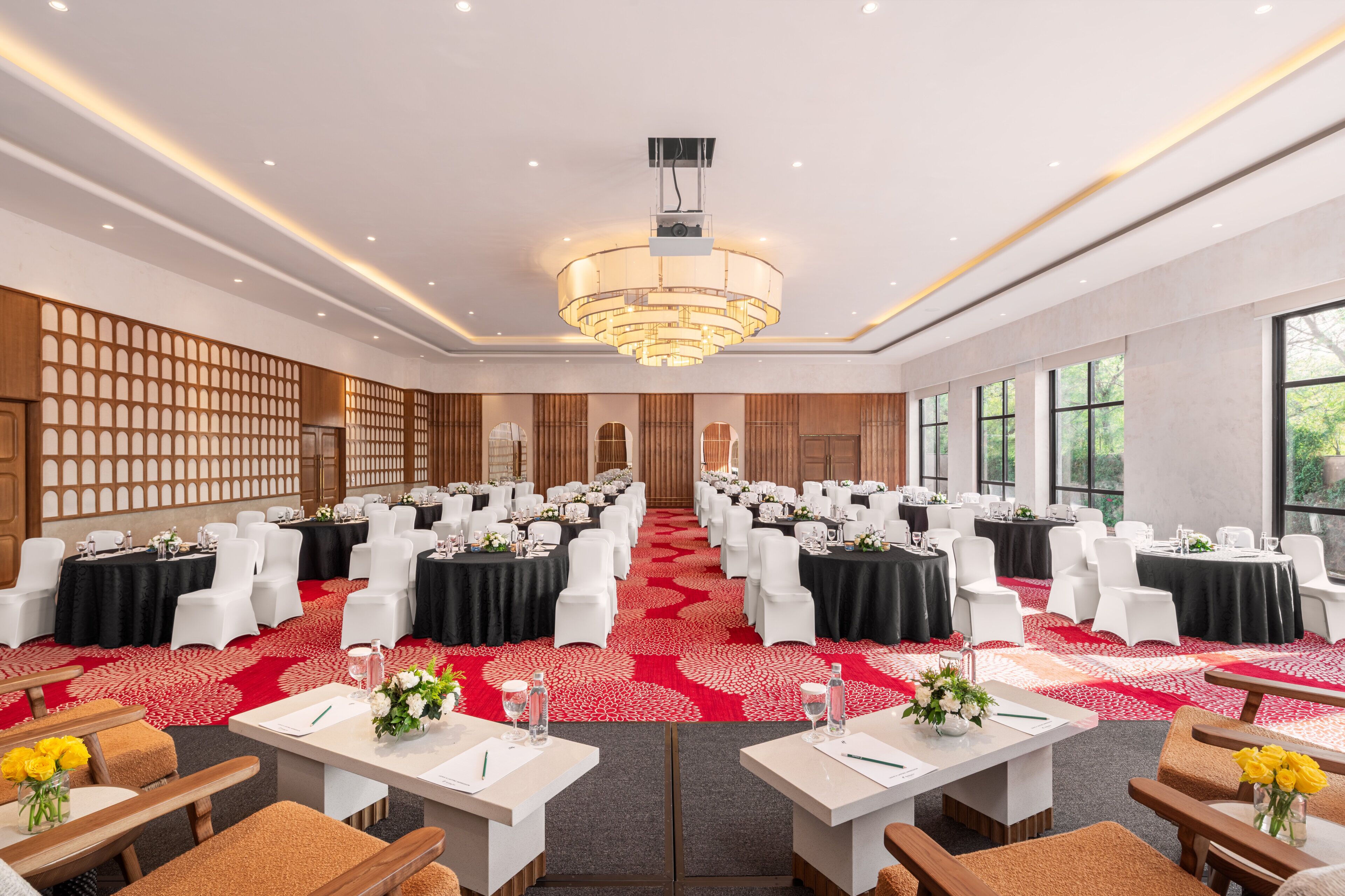 A conference room with rows of tables and chairs, a chandelier, and a red carpet.