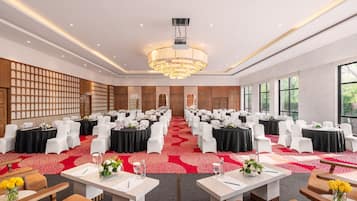 Un salón de conferencias con filas de mesas y sillas, una araña y una alfombra roja.
