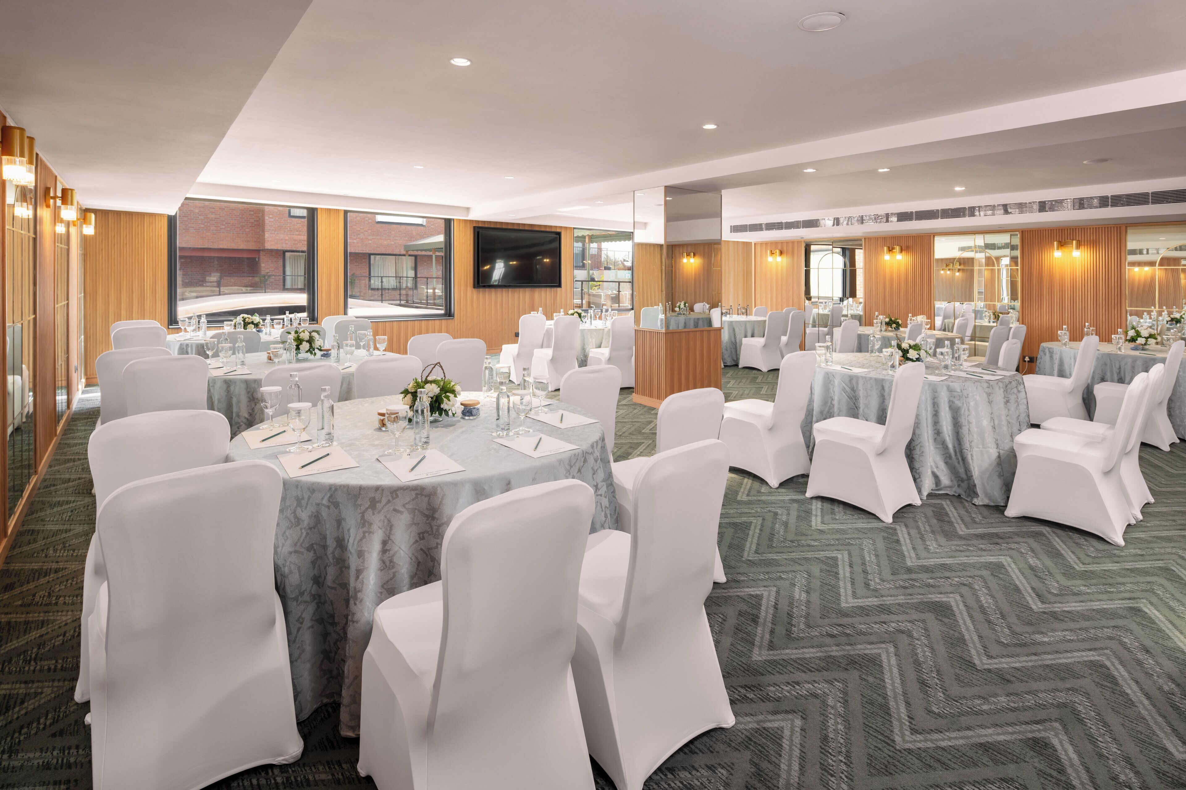 A conference room with round tables, white chairs, and a large screen.