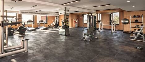 A spacious gym with various exercise equipment, large windows, and a modern design.