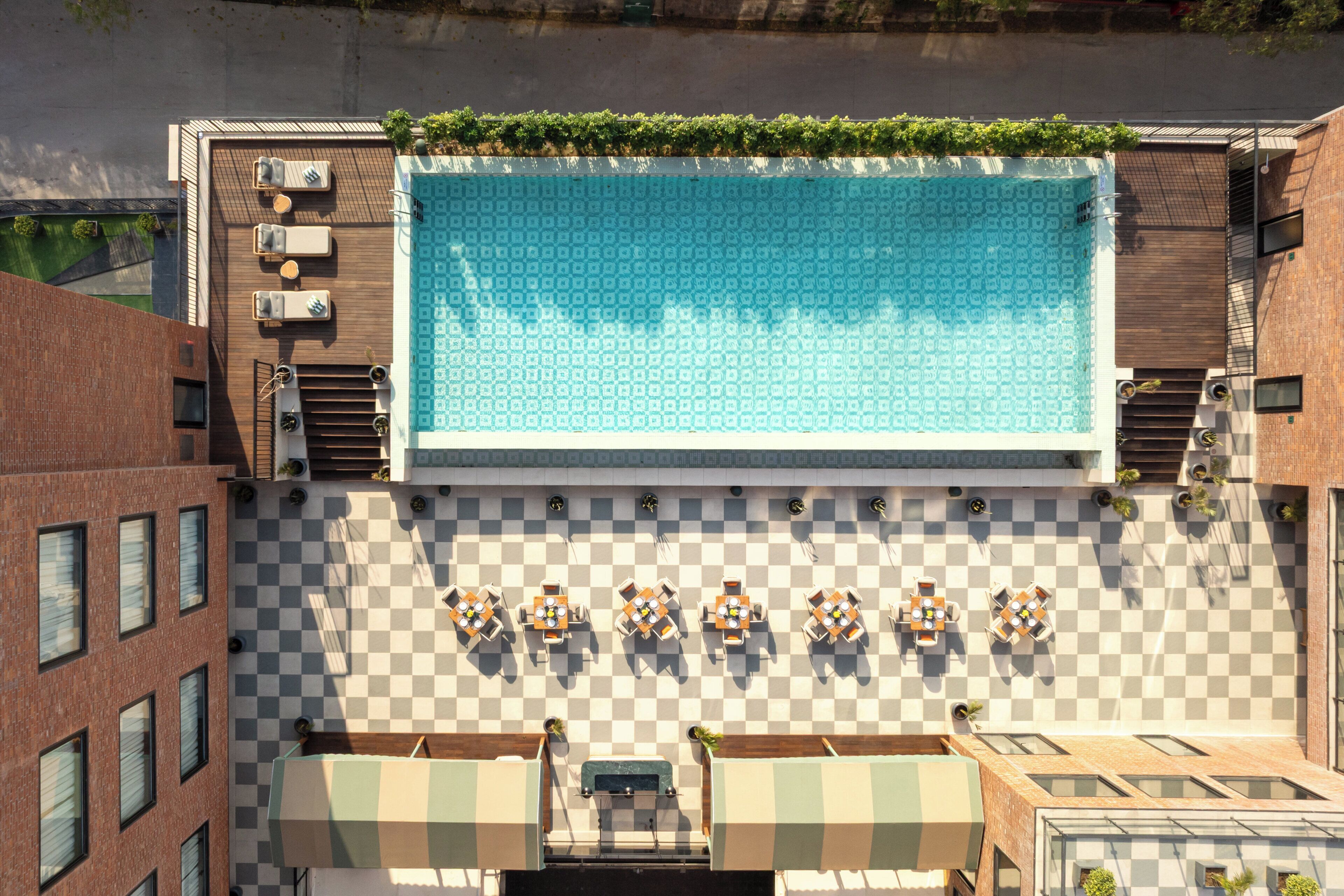 Vue aérienne d’un espace piscine sur le toit, avec un sol à carreaux, des chaises longues et une grande piscine.