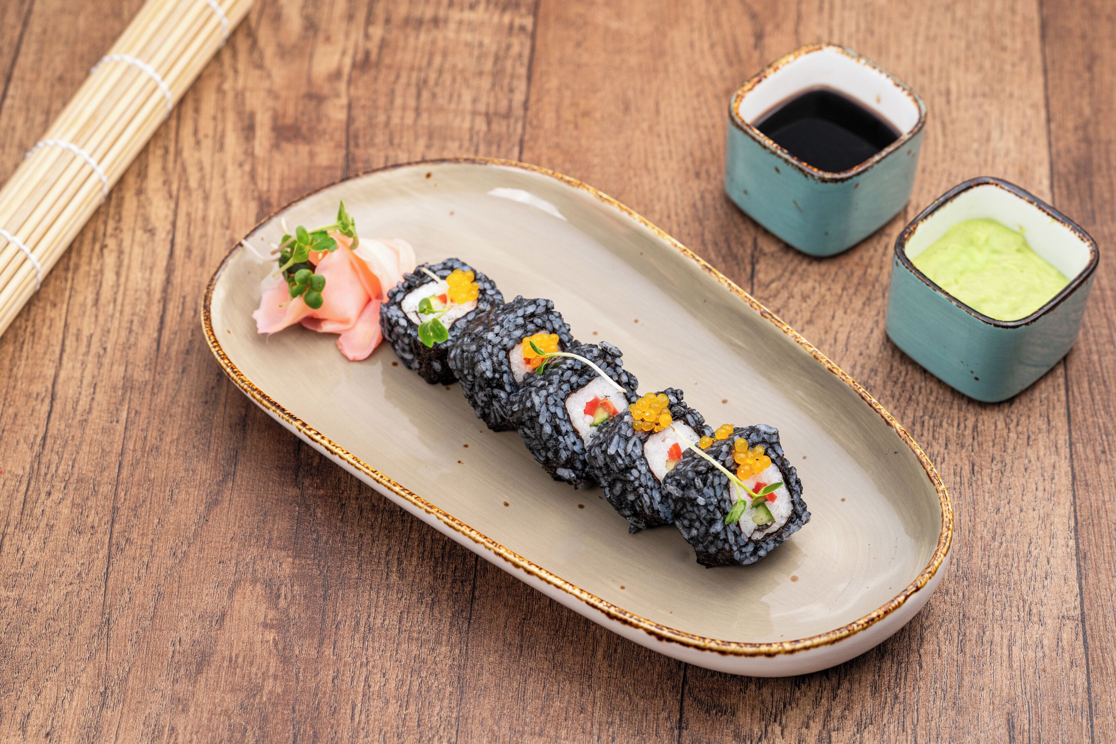 A plate of sushi with two small bowls of soy sauce and wasabi.