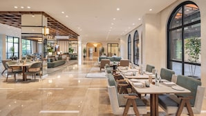 A spacious hotel lobby with a modern design, featuring a long dining table, comfortable seating, and large windows offering views. - Holiday Inn Gurgaon NH8 by IHG (Gurugram)