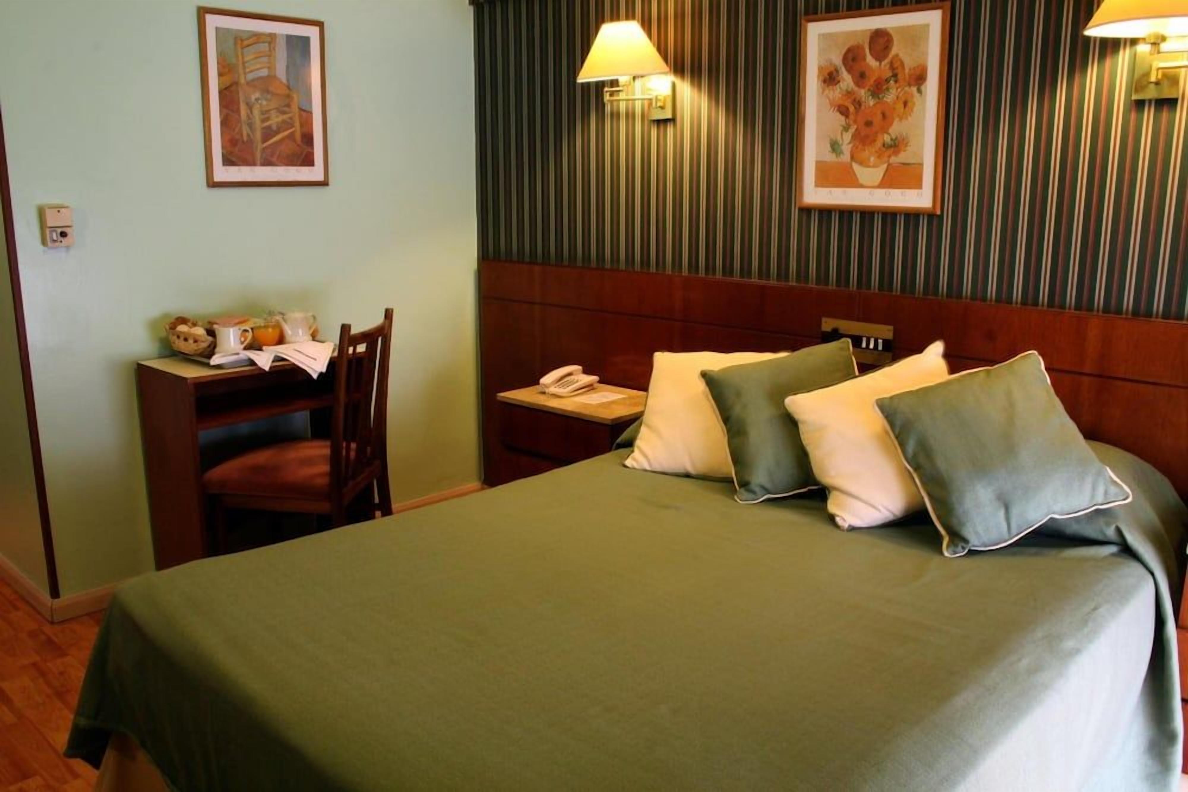 A hotel room with a bed, bedside table, lamp, and a chair.