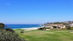Um campo de golfe costeiro com vista para o oceano e uma área residencial ao fundo.