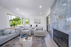 Una sala de estar moderna con chimenea, sofás grises, una mesa de centro y ventanas grandes.