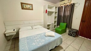 Une chambre à coucher avec un lit, un fauteuil vert, une petite table et une armoire.