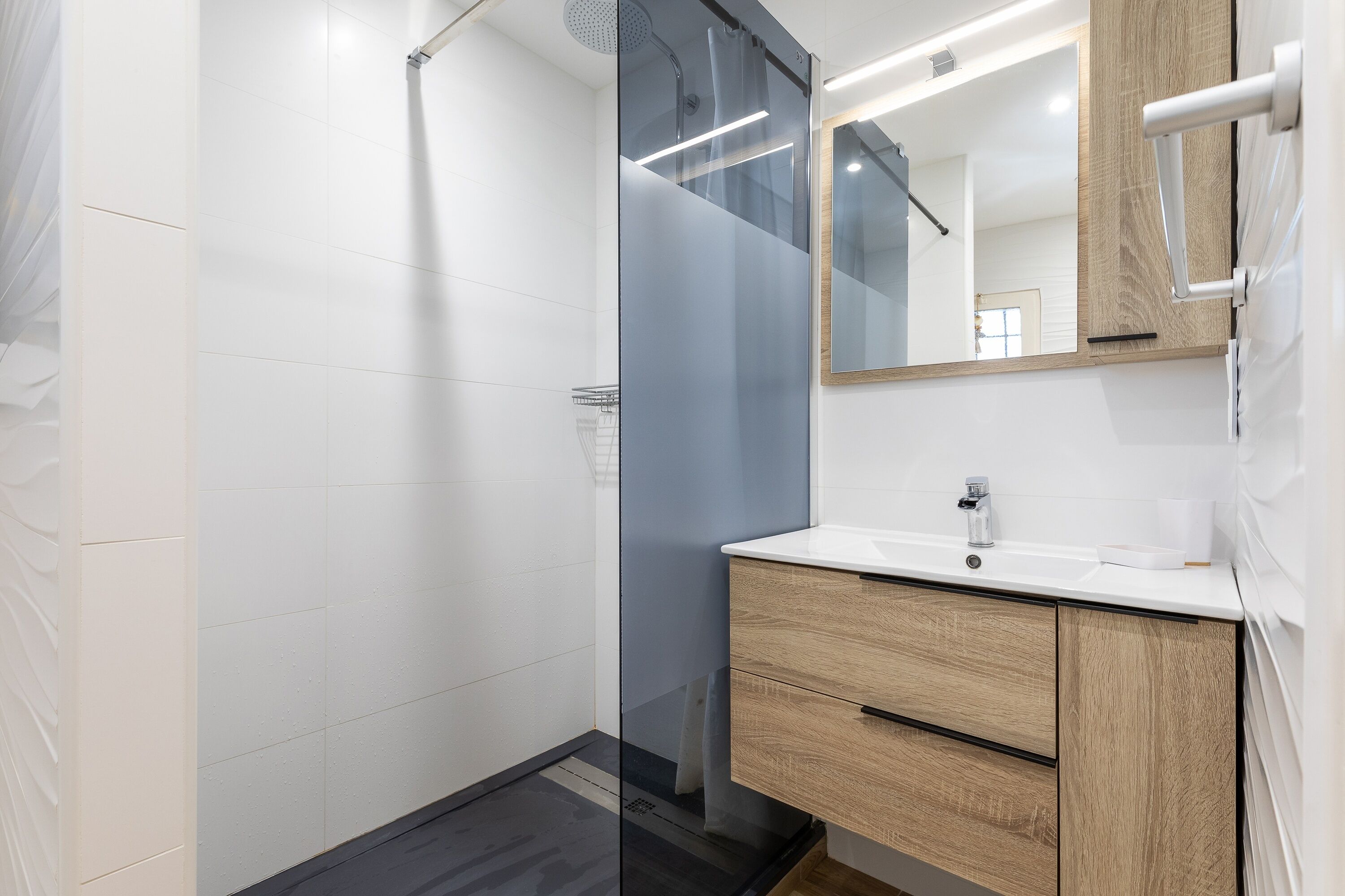 A modern bathroom with a glass shower enclosure, a wooden vanity with a mirror, and a white sink.