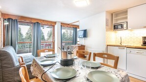 A dining area with a table set for four, a microwave, and a dishwasher in the kitchen area. - Joubarbes - Station à pied (Chamrousse)