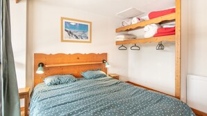 A bedroom with a wooden headboard, a bed with a polka dot duvet, a nightstand with a lamp, a shelf with folded clothes, and a framed picture on the wall. - Joubarbes - Station à pied (Chamrousse)