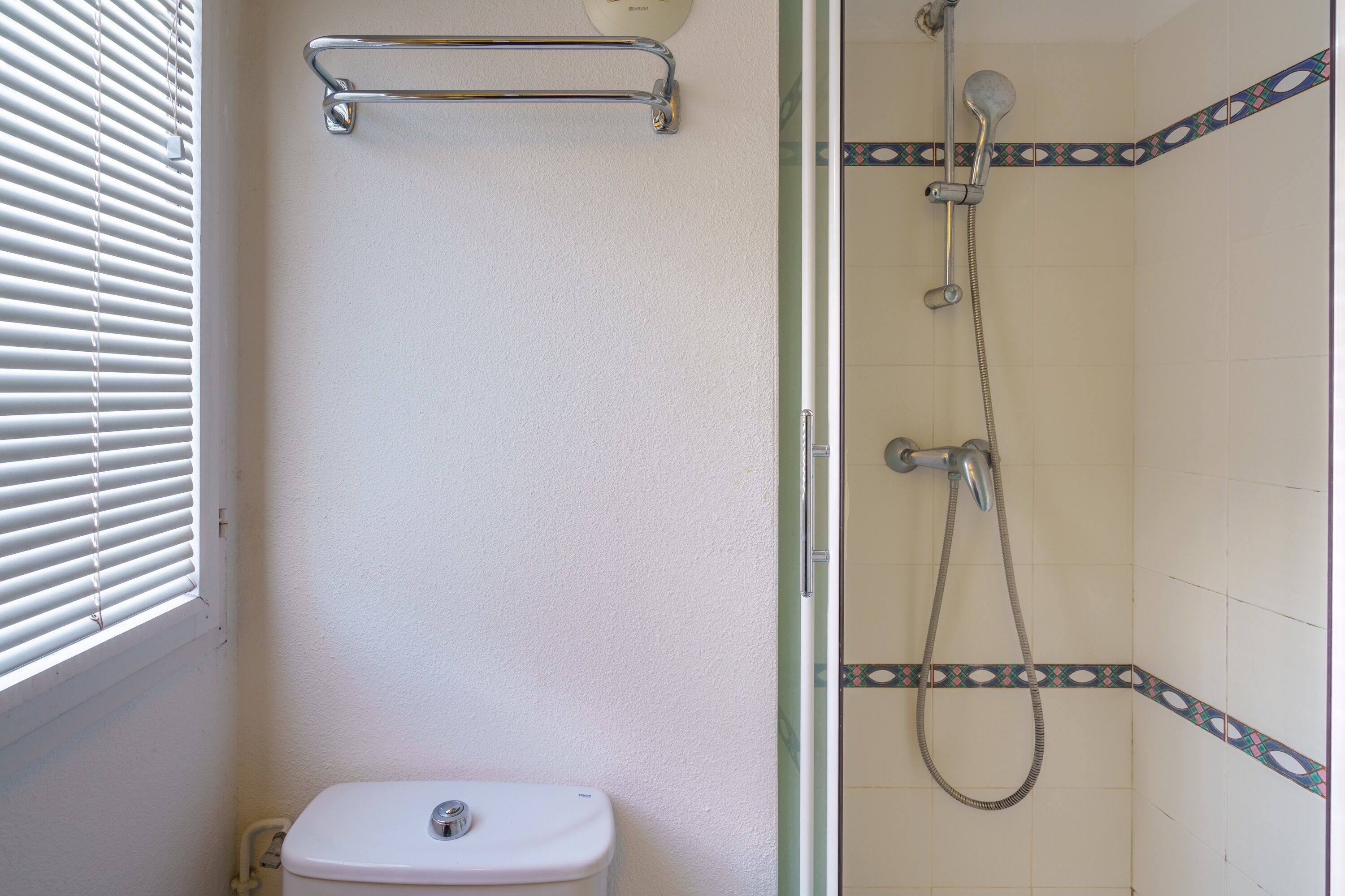 Un baño con inodoro, ducha y un soporte para toallas.
