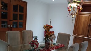 A dining area with a glass-top table, beige chairs, a floral centerpiece, and a wooden cabinet.