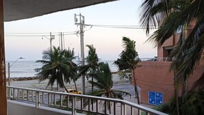 A balcony with a view of the beach, palm trees, and a brick building.