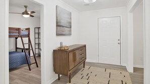 Un dormitorio con una cama individual superpuesta, un aparador de madera, un ventilador de techo, un cuadro y una puerta.