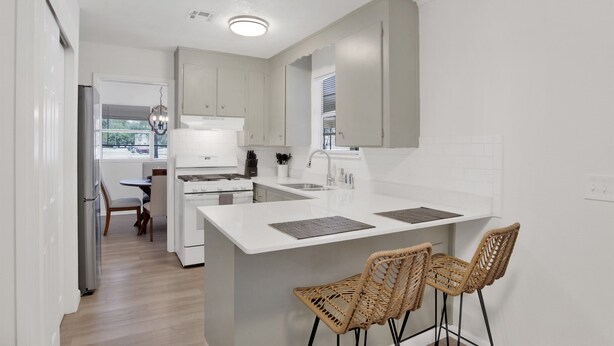 Una cocina moderna con armarios blancos, una isla central con taburetes altos y un comedor con mesa y sillas.