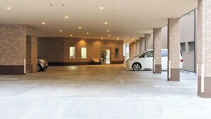 A covered parking area with brick walls, a bench, and cars parked inside. - Hotel Hayashiya Ishinomaki (Isinomaki)