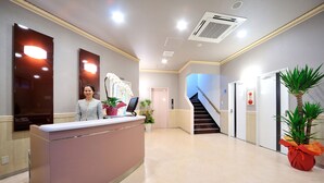 A reception desk with a woman standing behind it, a staircase, and a potted plant. - Hotel Hayashiya Ishinomaki (Isinomaki)