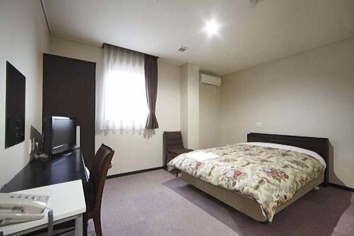 Une chambre d’hôtel équipée d’un lit, d’un bureau, d’une chaise, d’une télévision et d’une fenêtre avec des rideaux.