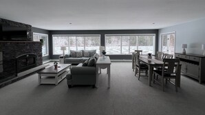 Una sala moderna con chimenea, un sofá, una mesa de comedor con sillas y ventanas amplias que ofrecen vistas a un paisaje nevado.