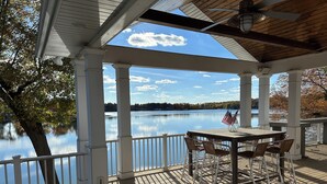 A covered deck with a table and chairs, overlooking a calm lake with trees and a clear sky. - Pine Lake Cottage with Views (Plainwell)
