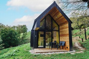 A modern wooden cabin with a large glass front, a wooden deck, and a scenic hillside background. - Jarica, modern cottage on Tri Vile estate with an amazing view (Šmarje pri Jelšah)